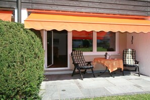 Um pátio externo com duas cadeiras e uma mesa, cerca de madeira e um arbusto.