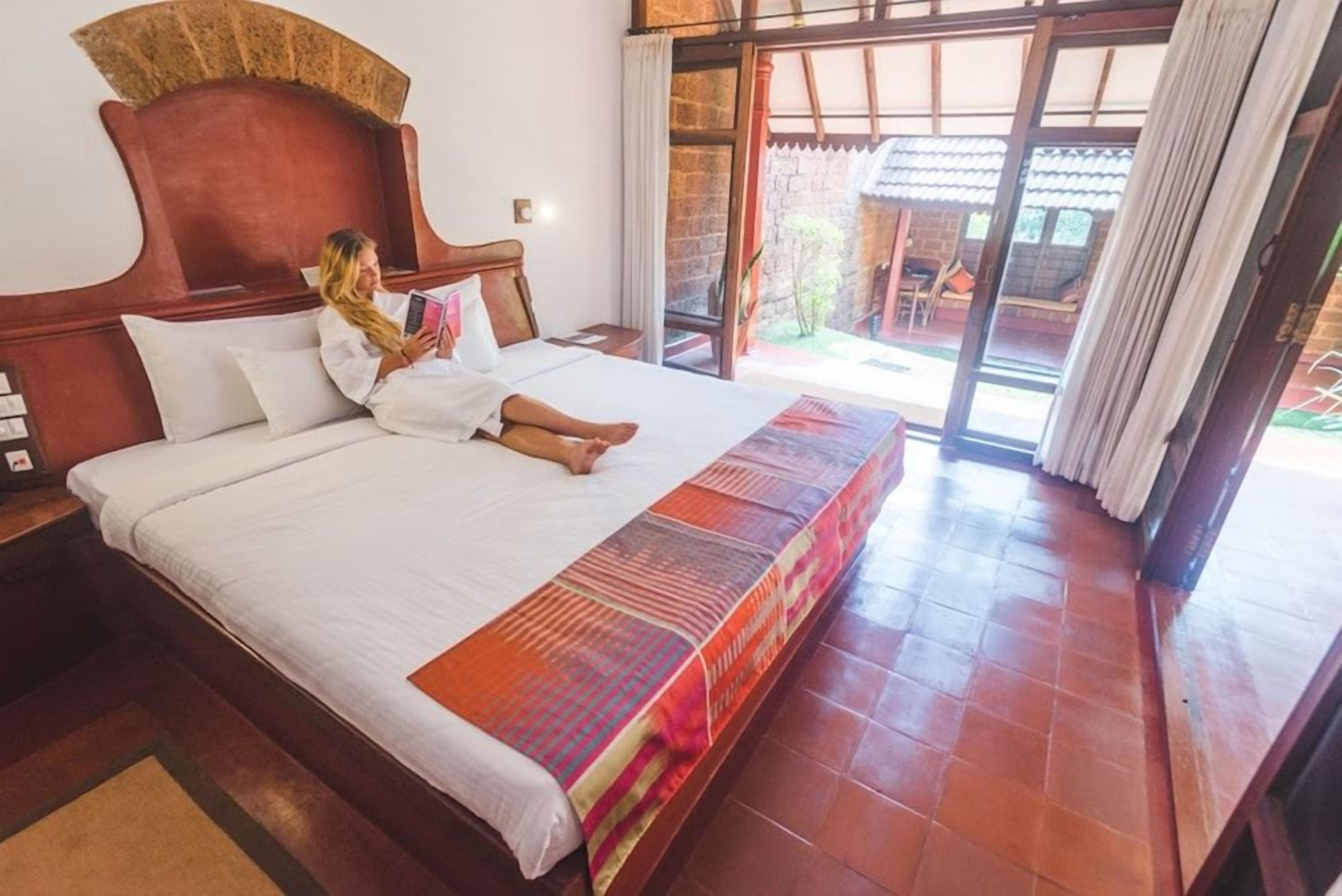 A hotel room with a large bed, a wooden headboard, and a view of a courtyard through a sliding glass door.