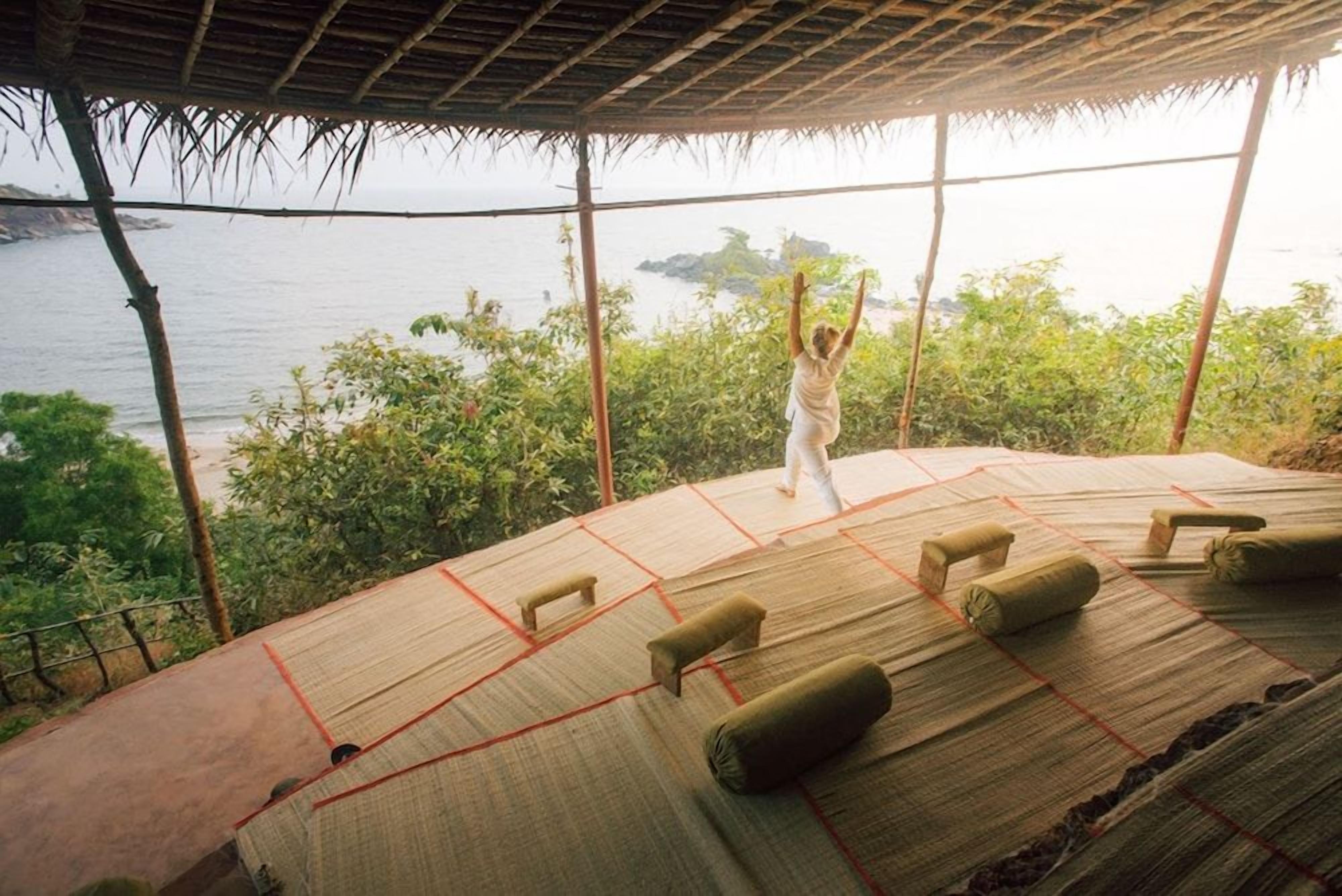 A person performing yoga on a mat with a view of the sea and greenery.