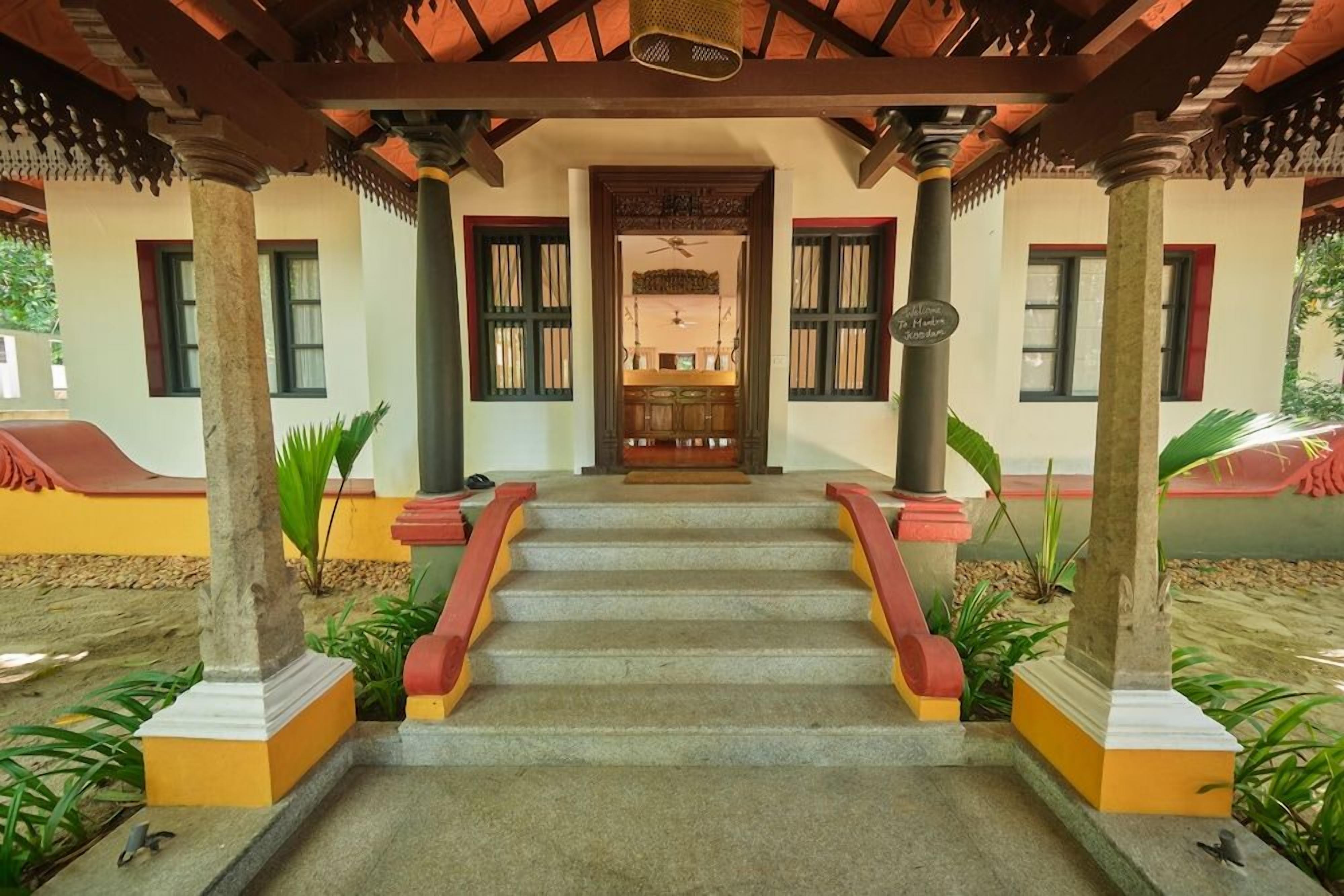 A staircase leading to a door with a sign above it, flanked by columns and plants.