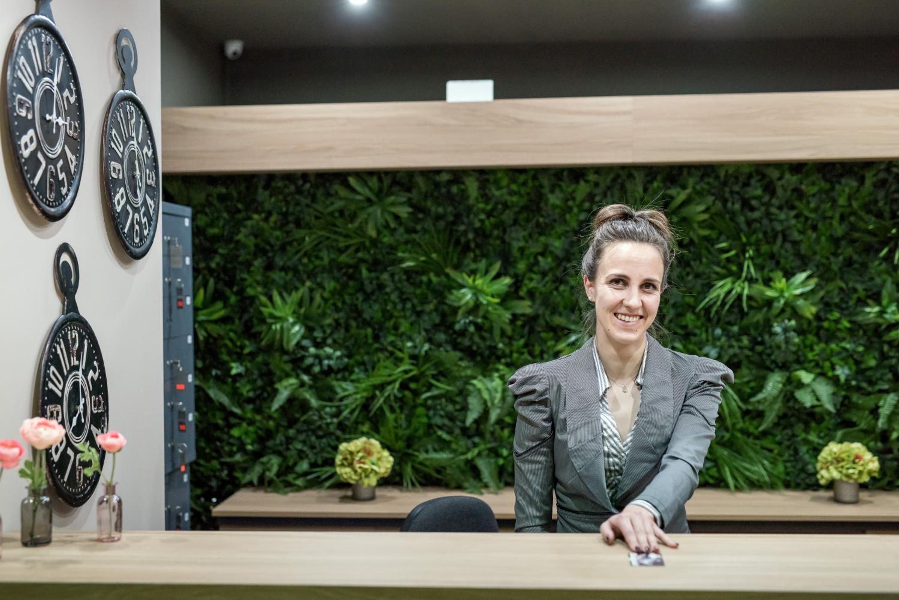 A reception desk with a modern design, a green wall with plants, and decorative clocks.