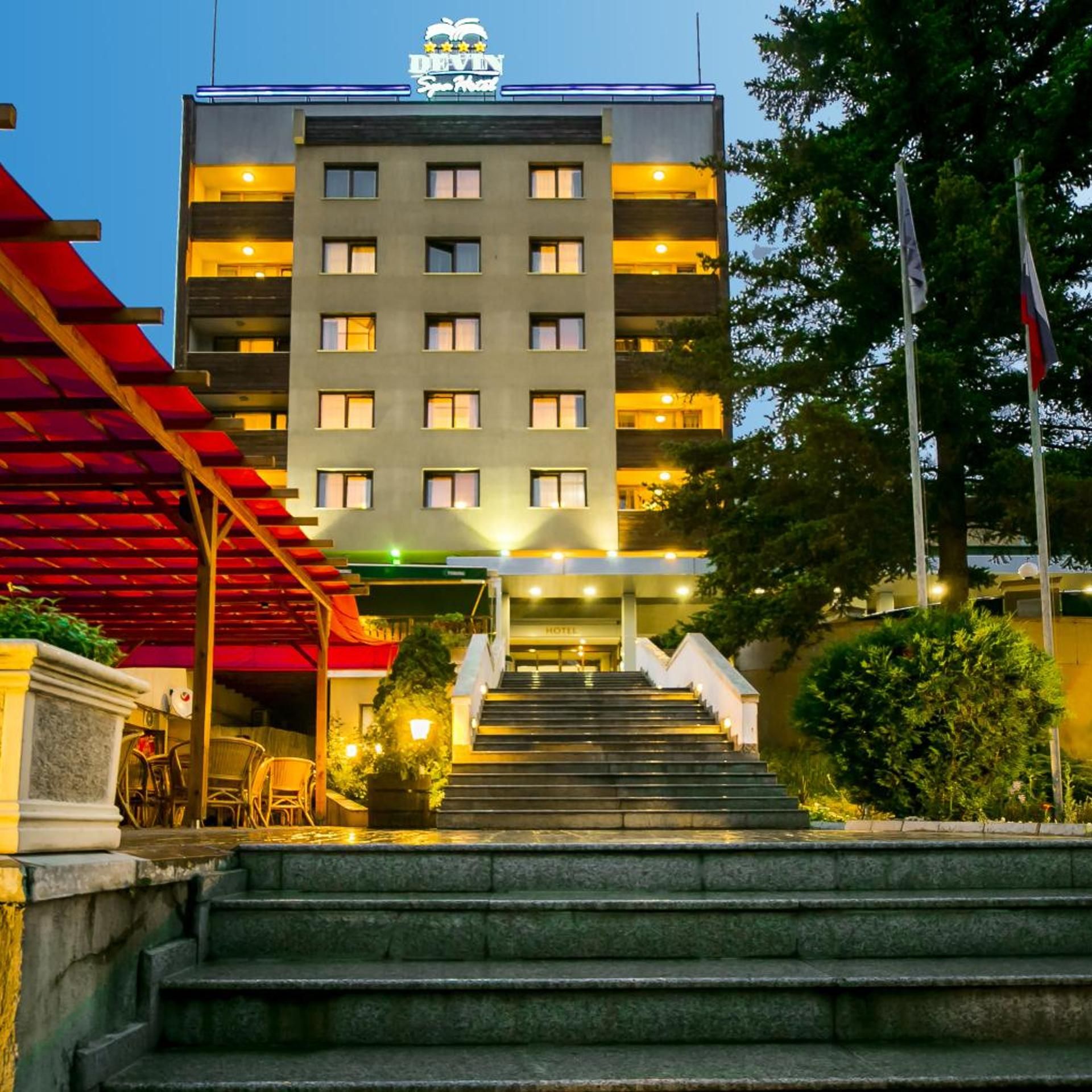 A hotel entrance with a staircase leading to the lobby, a covered outdoor seating area, and a flagpole.