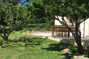 Ein Garten mit einer Holzbank, einem Baum und einem Gebäude im Hintergrund.