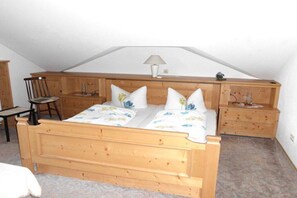 Quarto com cama de madeira, duas mesas de cabeceira, uma cadeira e um abajur.