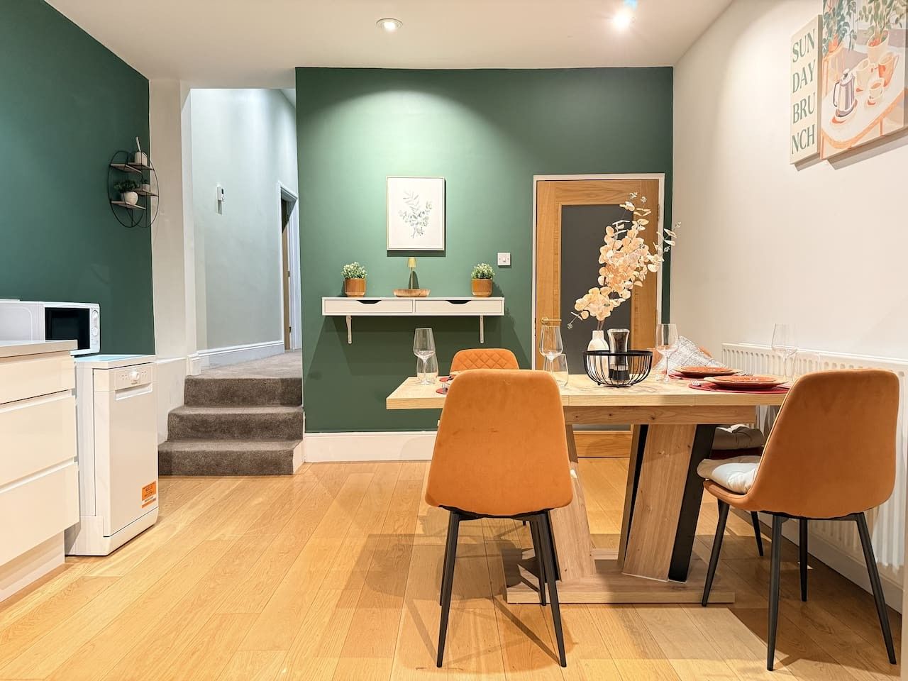 A dining area with a wooden table and two orange chairs, a white refrigerator, and a microwave.