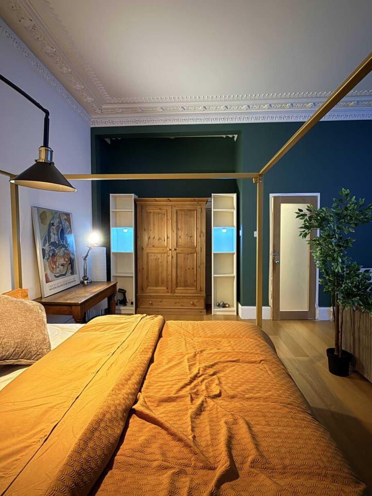 A bedroom with a bed, a desk, a lamp, a wardrobe, and a door.