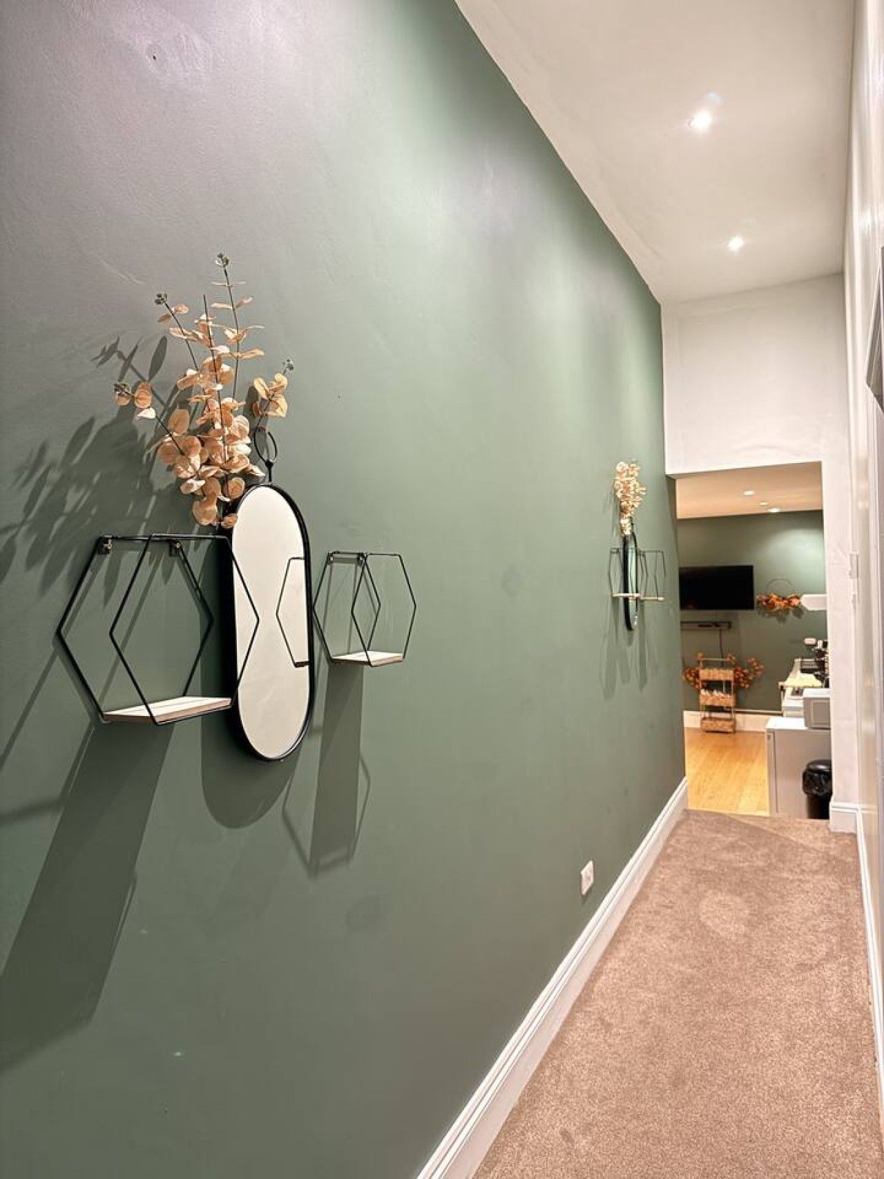 A hallway with a green wall, a mirror, and geometric wall art.
