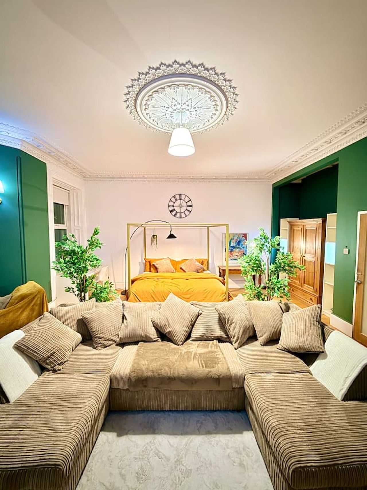 Une chambre à coucher avec un grand lit, un médaillon décoratif au plafond, une horloge et un mur vert.
