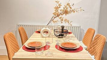 A dining table set for brunch with six chairs, a vase with dried flowers, and a wall art piece above.