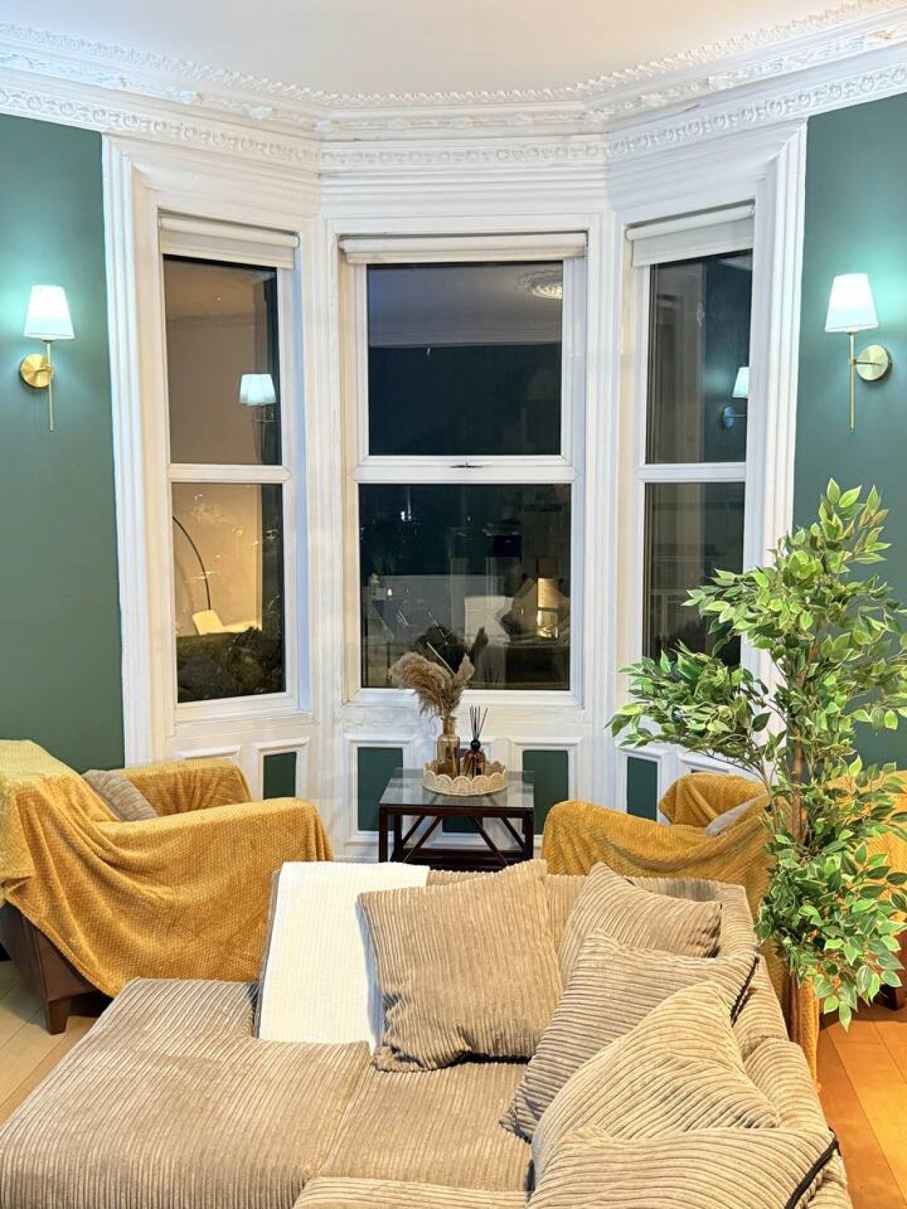 A room with a large bay window, a sofa, a small table, and a potted plant.