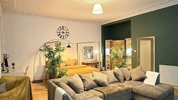 A living room with a sectional sofa, a floor lamp, a clock on the wall, and a ceiling light fixture.