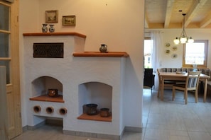 A room with a fireplace, wooden beams, a dining area with a table and chairs, and a window with curtains. - Holiday home in Allgäu with 3 bedrooms (Lechbruck am See)