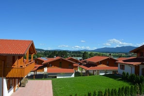 A row of wooden houses with red-tiled roofs, a grassy lawn, and a mountainous backdrop. - Holiday home in Allgäu with 3 bedrooms (Lechbruck am See)