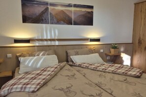 A bedroom with two beds, a wooden headboard, wall-mounted lamps, and a mountain landscape painting above the beds. - Holiday home in Allgäu with 1 bedroom (Lechbruck)