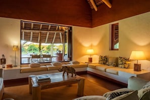 A cozy living room with a sofa, a coffee table, and a window overlooking a garden. - Zebras Crossing Private Game Lodge (Modimolle)