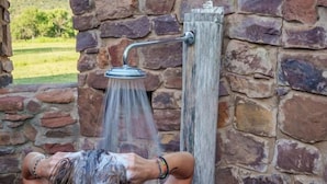 Une personne se douchant dans une cabine de douche en pierre, avec un poteau en bois rustique.