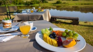 Een tafel gedekt met een fruitschaal, een glas sinaasappelsap en een toetje bij een tafel aan het meer.
