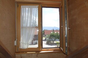 Ein Zimmer mit Holzvertäfelung, einem Fenster mit Vorhang und Blick auf eine Wohngegend mit Häusern und einem Berg in der Ferne.