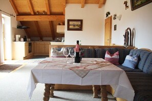 Ein gemütliches Wohnzimmer mit Esstisch für Zwei, einer Couch mit Kissen und einer Küche im Hintergrund.