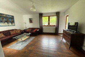 Ein Wohnzimmer mit braunem Ledersofa, einem Couchtisch, einem Fernseher auf einer Holzkommode und einem Bild an der Wand.