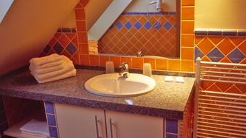 Un baño con techo inclinado, un lavamanos, un espejo y paredes de azulejos.