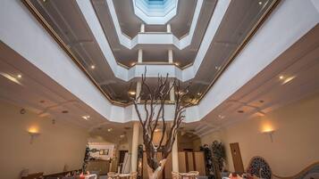 Un vestíbulo de hotel con un atrio central, varias zonas de estar y una escultura decorativa de un árbol.
