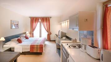 Habitación de hotel con cama, mesita de noche, lámpara, televisor y kitchenette.