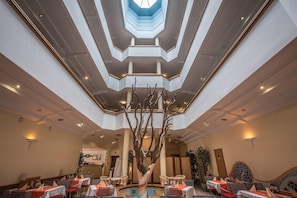 Et hotel lobby med et centralt atrium, flere siddeområder og en dekorativ træskulptur.