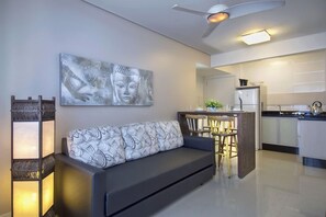 Una sala de estar moderna con un sofá, un cuadro de Buda montado en la pared y una zona de cocina al fondo.