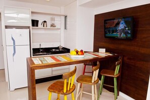 Una cocina compacta con un refrigerador blanco, estufa y una mesa de madera con sillas. Un televisor está montado en la pared.