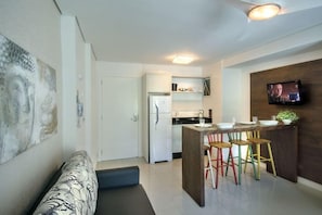 A modern kitchen with a built-in island, a dining area with colorful stools, and a flat-screen TV mounted on the wall. - Pousada Bora Bora (Bombinhas)