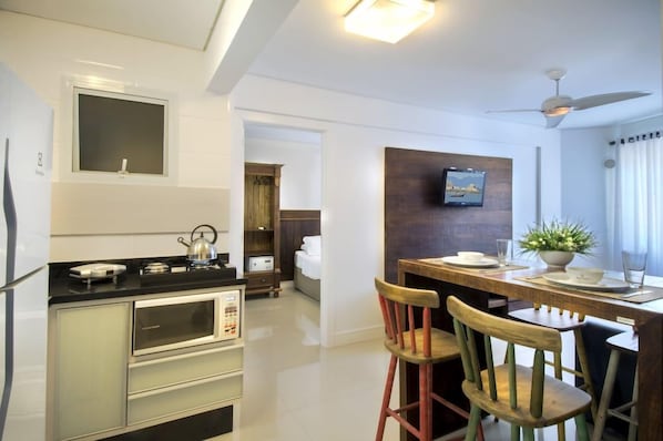 A modern kitchen with a dining area, a television mounted on the wall, and a ceiling fan. - Pousada Bora Bora (Bombinhas)