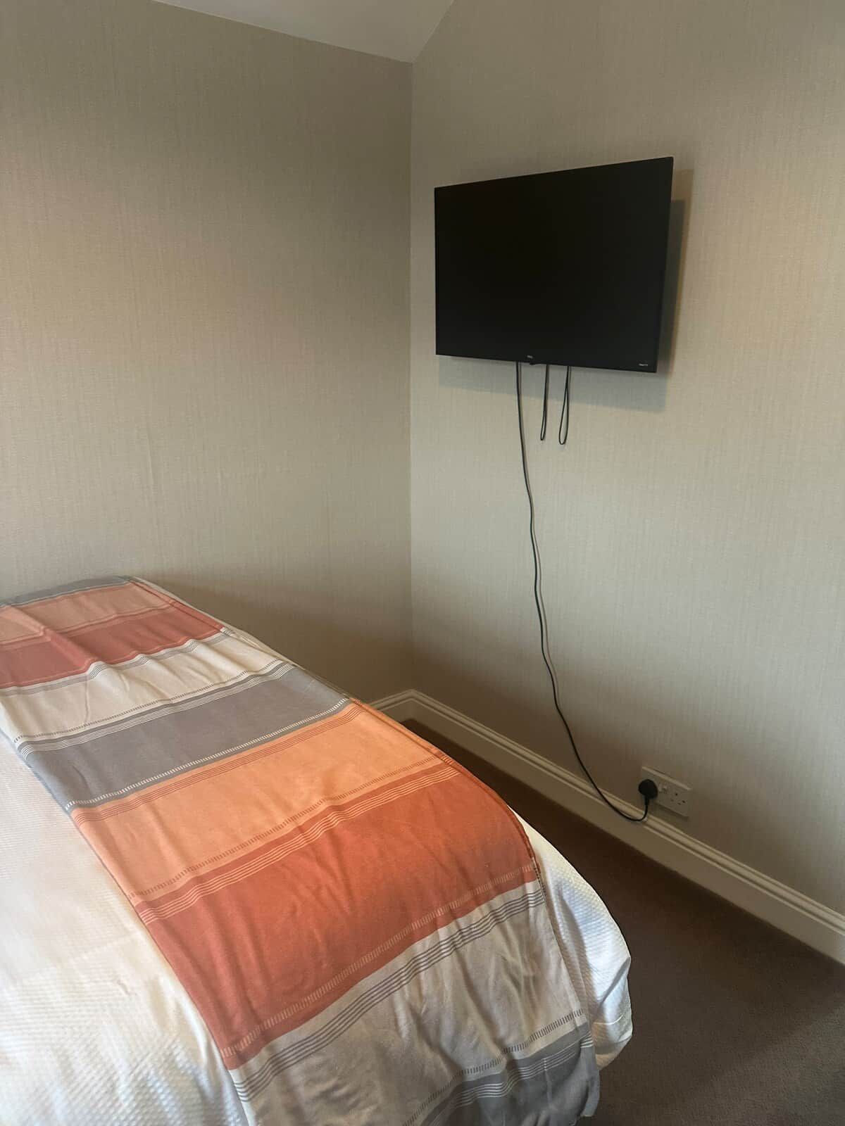 A bedroom with a bed, a television mounted on the wall, and a power outlet.