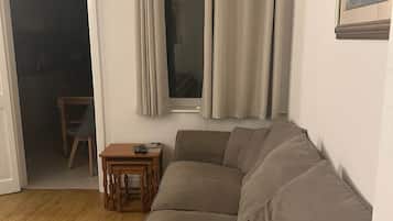 En stue med en beige sofa, et lille træbord og et vindue med gardiner.