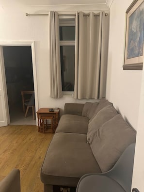 Una sala de estar con un sofá color beige, una mesita de madera y una ventana con cortinas.