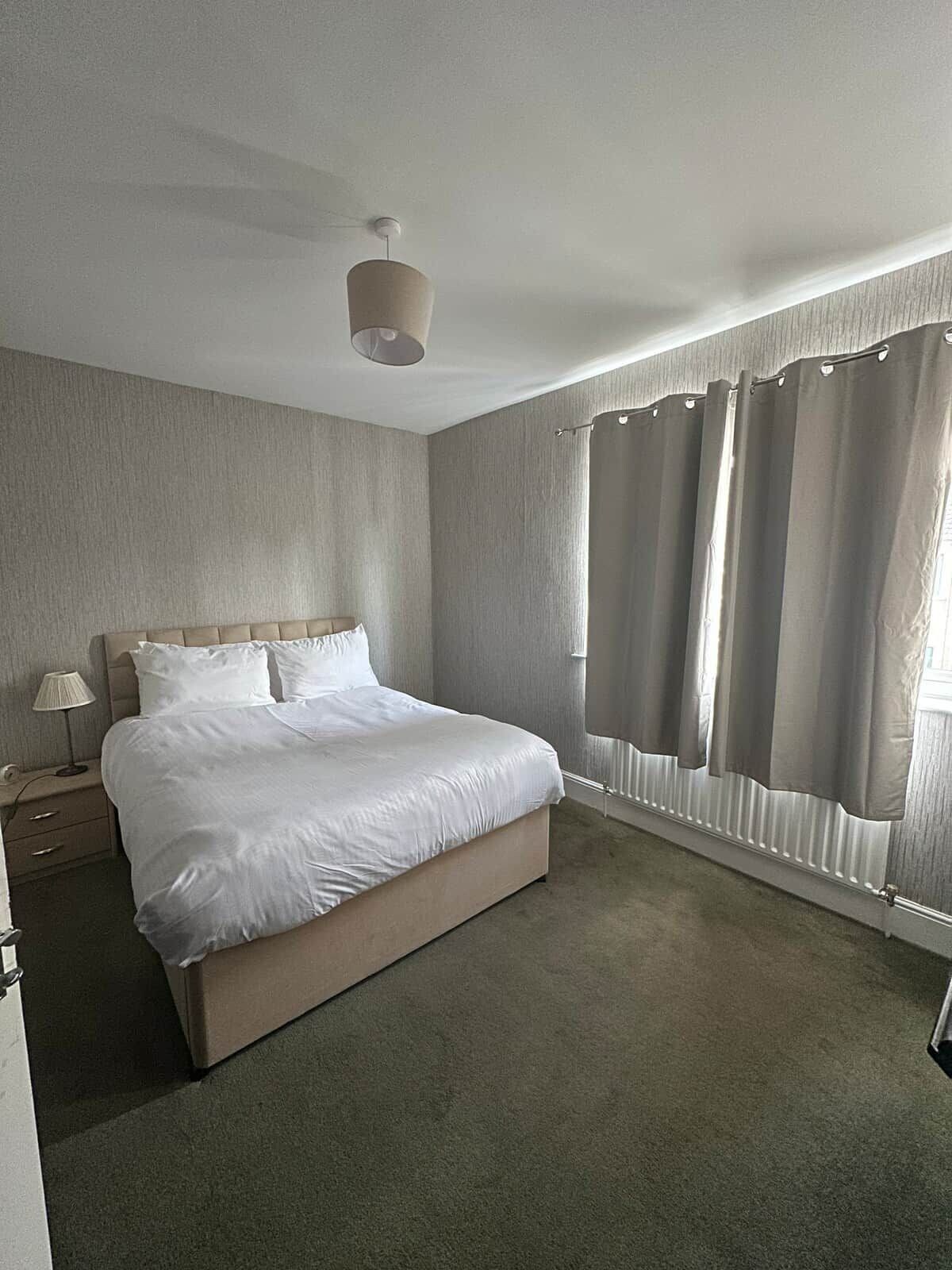 A bedroom with a bed, a nightstand, a lamp, and a window with curtains.