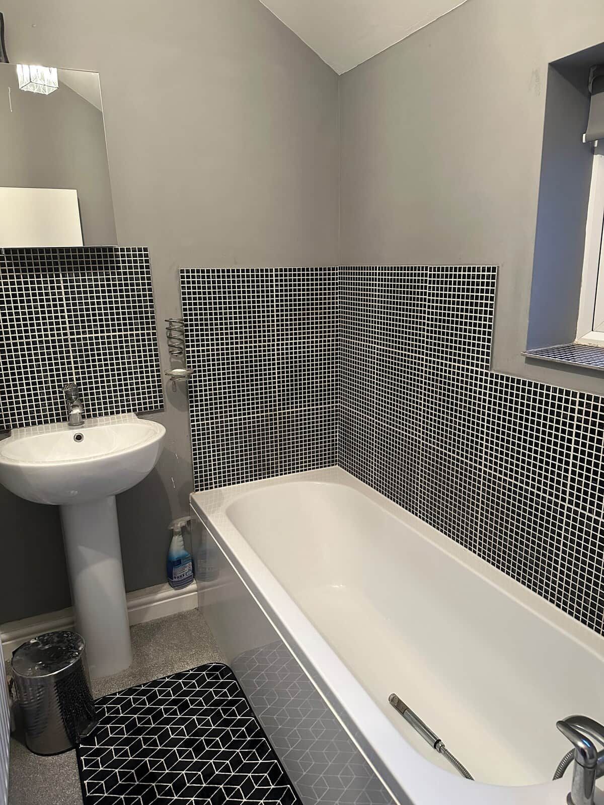 A bathroom with a white sink, a bathtub, and black and white patterned tiles on the walls.