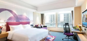 Habitación de hotel con una cama grande, un escritorio con silla, televisión y ventana con vista a la ciudad.