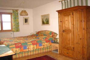 Um quarto com cama, guarda-roupa de madeira, janela com cortinas e um quadro na parede.