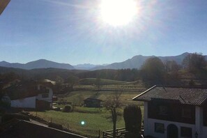 Paisaje rural con una casa, una construcción pequeña y montañas al fondo.