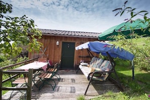 Una terraza de madera con una mesa, sillas, un banco y un área cubierta con un paraguas verde.
