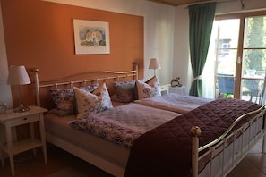 Un dormitorio con cama, dos mesitas de noche, una lámpara, un cuadro en la pared y una ventana con cortinas.