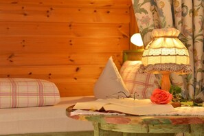 Ein gemütliches Zimmer mit einer Holzwand, einem Tisch mit Lampe, einem Buch, einer Brille und einer Rose.