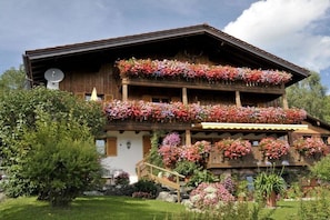 Ein Chalet mit mehreren Balkonen, die mit Blumen geschmückt sind, einer Satellitenschüssel und einem Steinfundament.