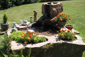A garden fountain with a stone structure, surrounded by potted plants and flowers. - Holiday apartment in Iggelbach with Wi-Fi (Iggelbach)