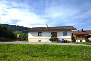 A two-story house with a tiled roof, a front porch, and a small garden area. - Holiday home in Steibis with swimming pool (Steibis)