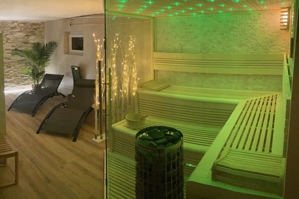 A spa room with a massage table, two lounge chairs, a small plant, and decorative lights.