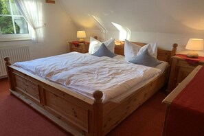 A wooden bed with white bedding, two bedside tables with lamps, a window with curtains, and a radiator. - Holiday home with 1 bedroom (Varel - Dangast)