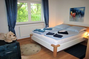 Ein Schlafzimmer mit einem Bett, einem Fenster, einem Heizkörper, einem Teddybären, einem Gemälde und einem Teppich.