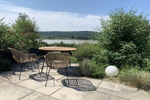 An outdoor seating area with a table and chairs, surrounded by greenery and overlooking a body of water. - Holiday apartment in Kronburg with sauna (Kronburg)